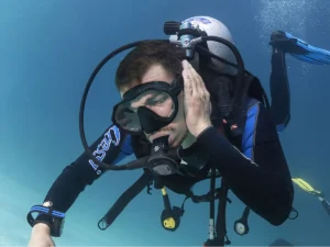 Buceador tocándose el oído bajo el agua con gesto de molestia durante una inmersión