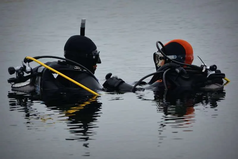 Persona principiante preparándose para bucear con apoyo de un instructor en aguas tranquilas