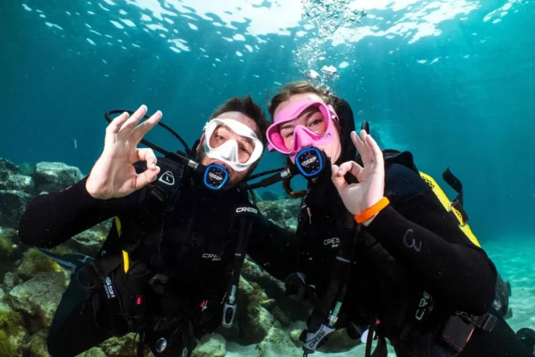 Two divers making the OK sign underwater during a beginner diving experience