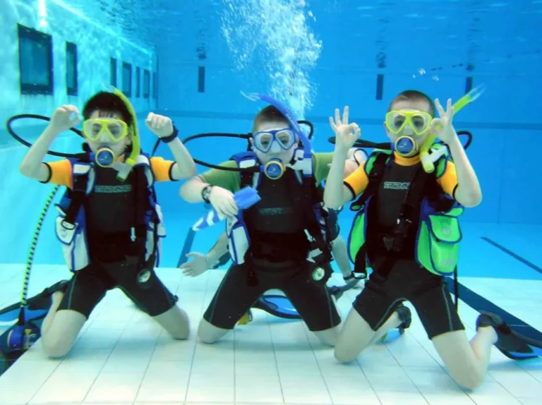 Tres niños aprendiendo a bucear y haciendo la señal de OK durante una práctica de buceo